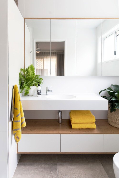 Phòng tắm có màu sáng chủ đạo cùng một chút màu của gỗ hài hoà, trang trí thêm vài chậu cây tinh tế. Phần bồn rửa thiết kế tối giản và dễ dàng vệ sinh.