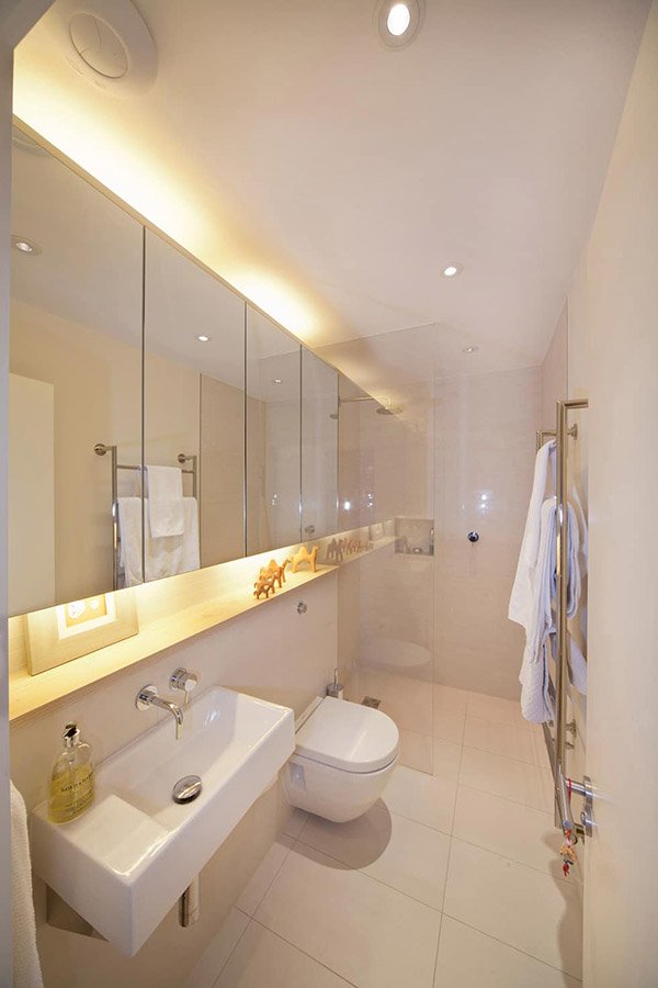 Phòng tắm có gương trải dài cùng bồn rửa mặt rộng, bồn cầu âm tường tiết kiệm diện tích bề ngang của phòng tắm. Đèn vàng trắng tạo không gian ấm cúng.